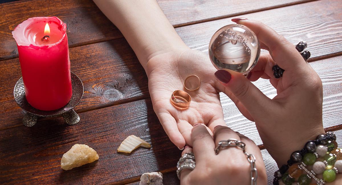 “Consulta esotérica con bola de cristal, anillos de boda y vela roja en un ritual de amor y adivinación espiritual”.